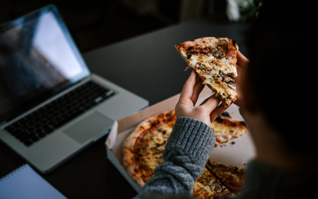 a woman eating pizza at desk with a laptop on it